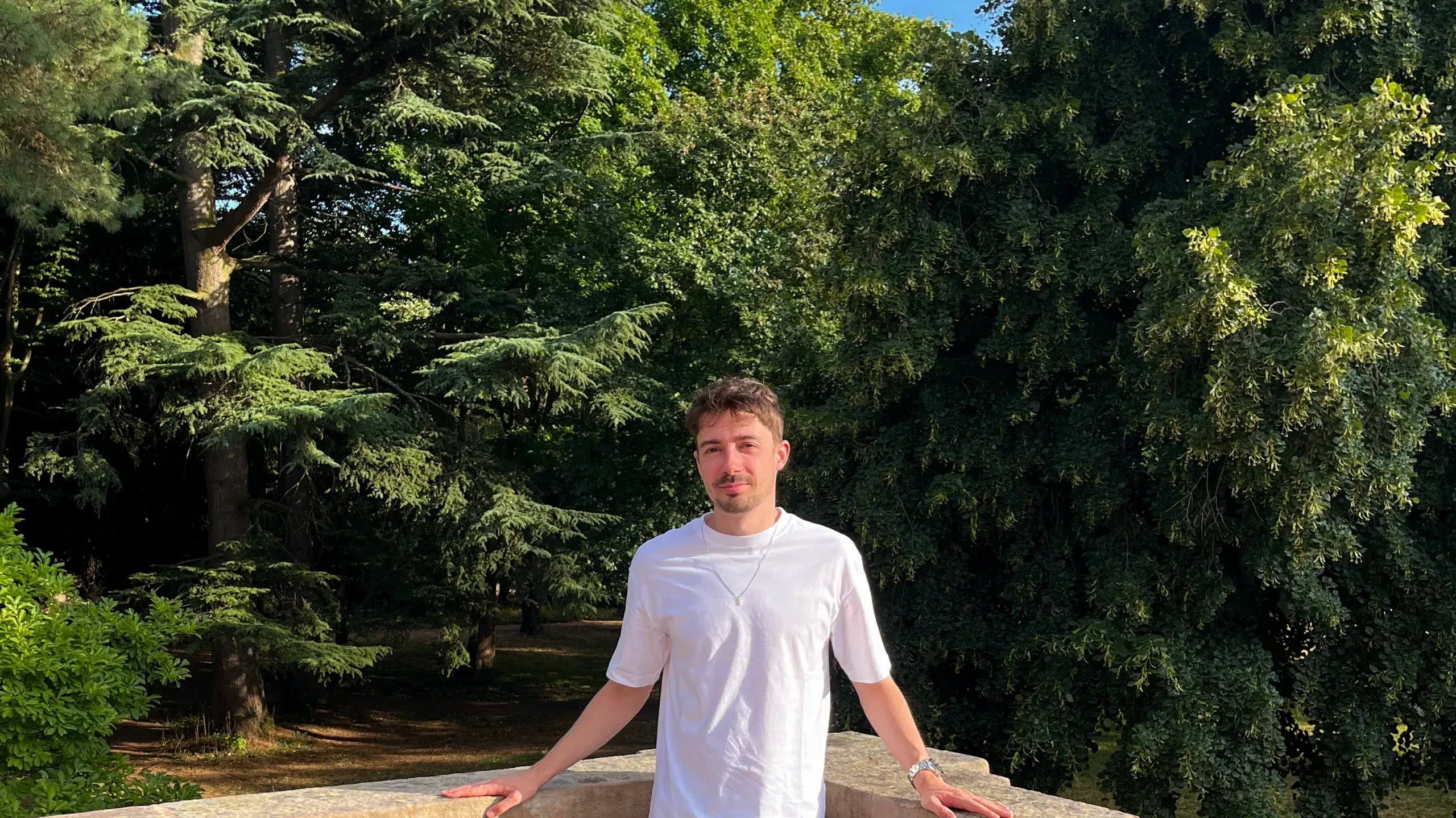 Homme brun adossé à une rembarde devant un jardin verdoyant